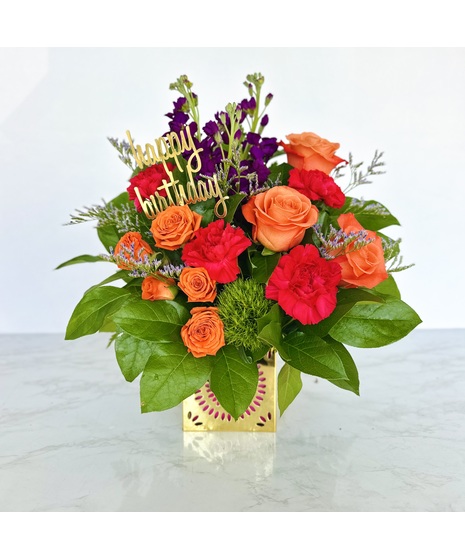 Flower bouquet of orange roses, fuchsia stock and pink carnations in a metallic cube vase.