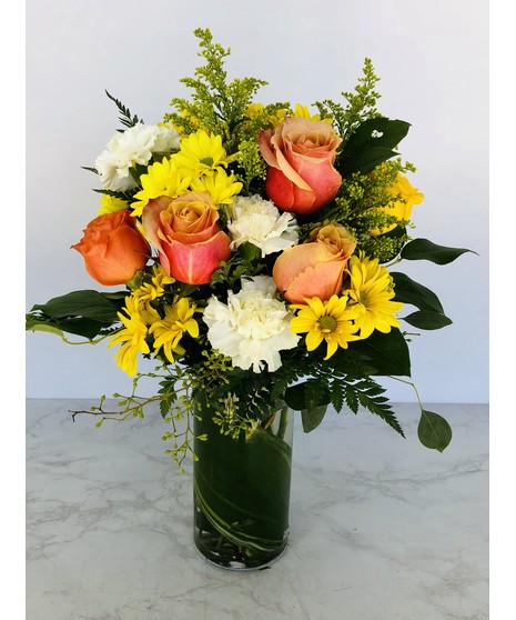 Orange and coral roses with yellow carnations and button mums in a glass vase.